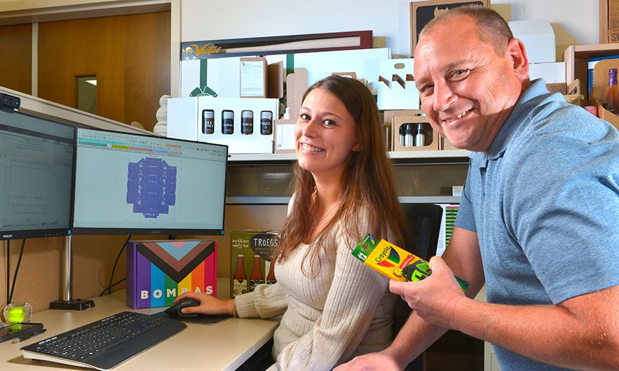 Two people working on a packaging design looking into the camera.